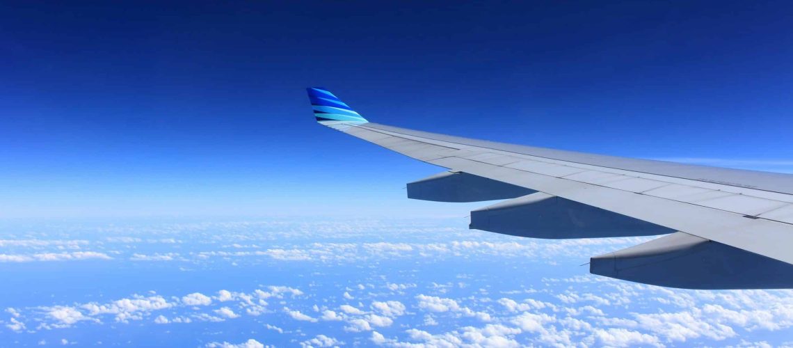 Scenic view of an airplane wing flying high above the clouds on a clear day.